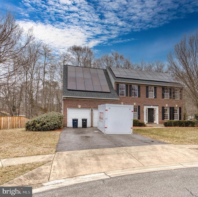 view of front of home featuring driveway, solar panels, a front lawn, a garage, and brick siding