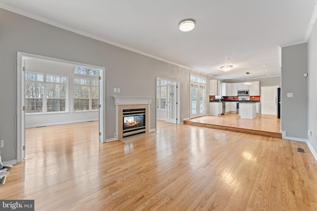 unfurnished living room featuring crown molding, a fireplace with flush hearth, light wood-style floors, and baseboards