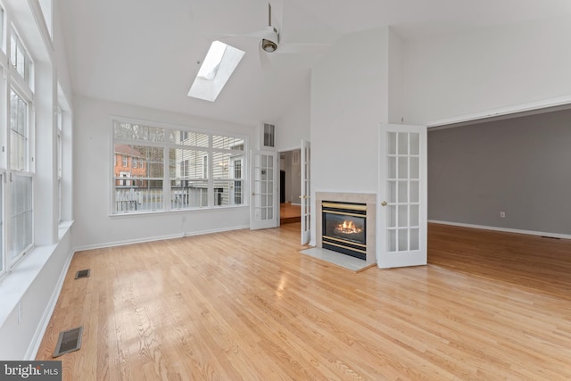 unfurnished living room featuring visible vents, wood finished floors, high vaulted ceiling, and a glass covered fireplace