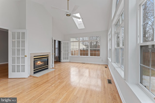 unfurnished living room featuring visible vents, baseboards, wood finished floors, a glass covered fireplace, and high vaulted ceiling