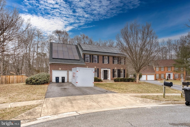 colonial-style house with driveway, fence, a front yard, brick siding, and solar panels