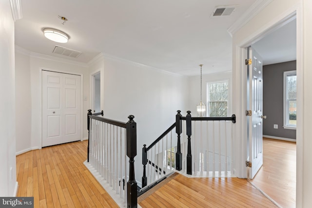 hallway with an upstairs landing, visible vents, ornamental molding, and hardwood / wood-style flooring