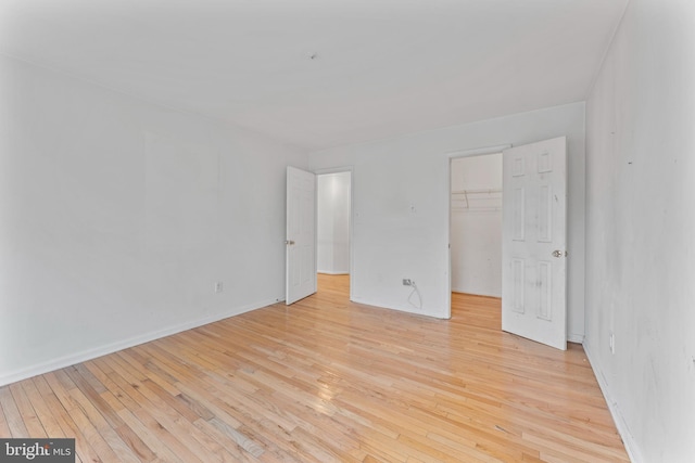 unfurnished bedroom with a closet, baseboards, a walk in closet, and light wood finished floors