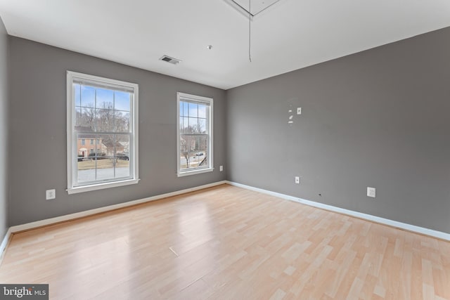 empty room featuring visible vents, attic access, baseboards, and wood finished floors