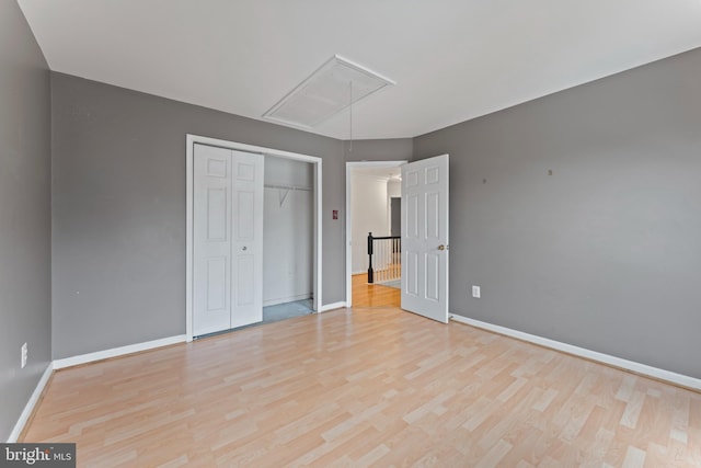 unfurnished bedroom with a closet, baseboards, attic access, and wood finished floors