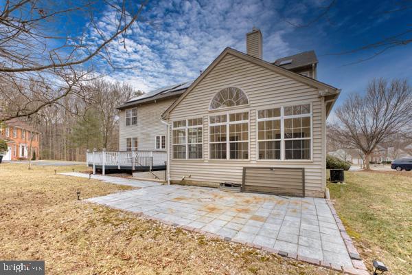 rear view of property with a yard, a sunroom, a wooden deck, a chimney, and a patio area