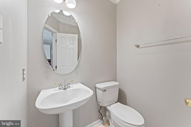 half bathroom with a sink, baseboards, and toilet