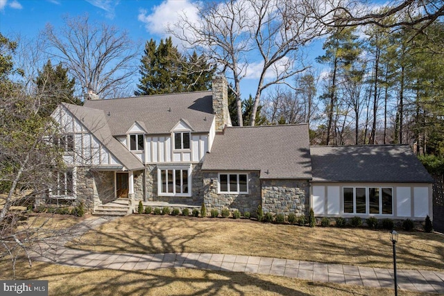 tudor-style house featuring stone siding, a chimney, stucco siding, and a front yard