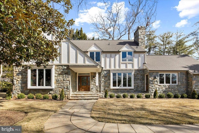 english style home featuring roof with shingles, a chimney, a front lawn, and stucco siding