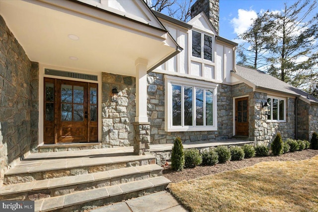 doorway to property featuring stone siding, a chimney, and covered porch