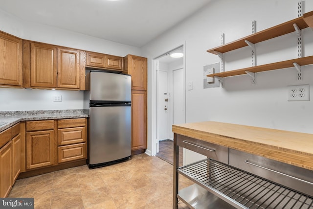 kitchen with open shelves, brown cabinetry, and freestanding refrigerator