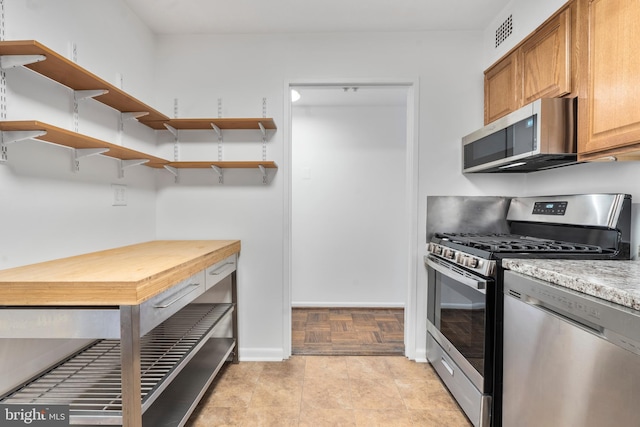 kitchen featuring stainless steel appliances, open shelves, visible vents, and baseboards