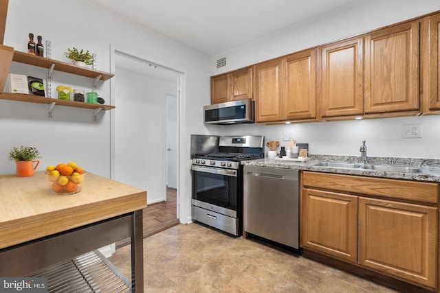 kitchen featuring visible vents, appliances with stainless steel finishes, brown cabinets, open shelves, and a sink