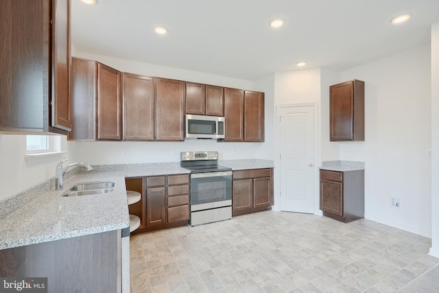 kitchen with light stone counters, stainless steel appliances, recessed lighting, dark brown cabinetry, and a sink