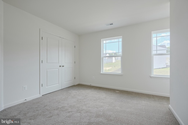 unfurnished bedroom featuring carpet floors, multiple windows, visible vents, and baseboards