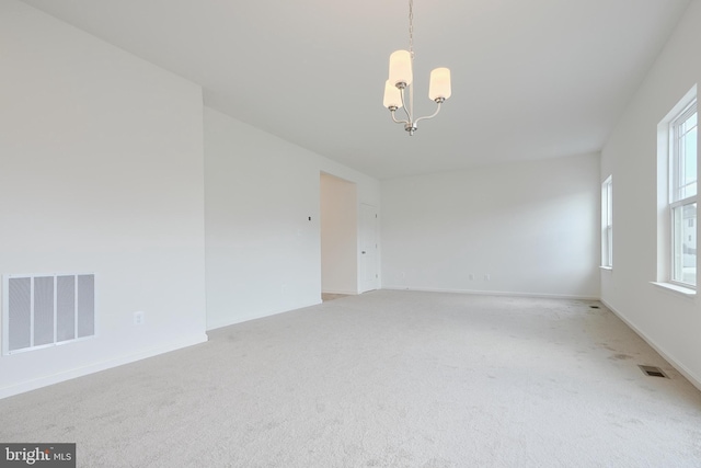 carpeted spare room with baseboards, visible vents, and a chandelier