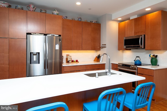 kitchen with a breakfast bar, a sink, light countertops, appliances with stainless steel finishes, and tasteful backsplash