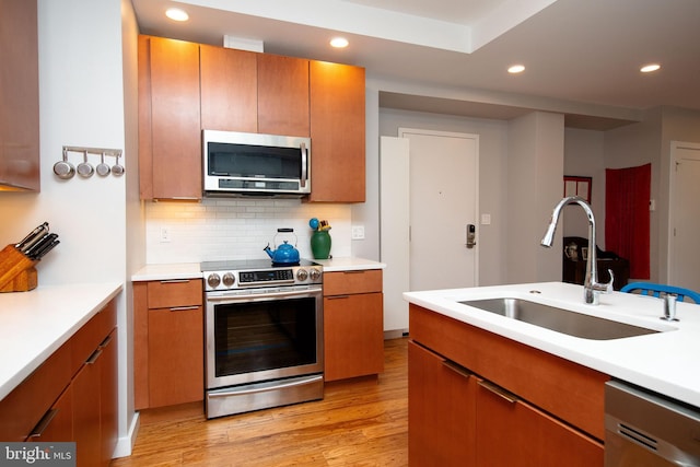 kitchen featuring stainless steel appliances, tasteful backsplash, light countertops, a sink, and light wood-type flooring