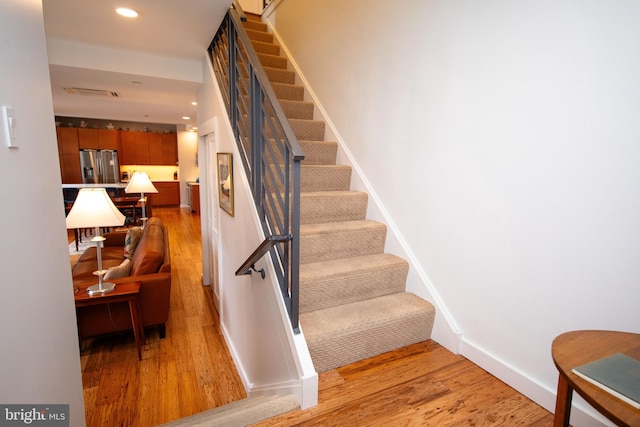 stairway with baseboards, visible vents, wood finished floors, and recessed lighting