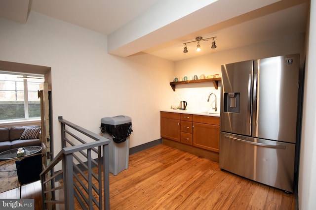 kitchen featuring light wood finished floors, stainless steel fridge, brown cabinetry, light countertops, and a sink