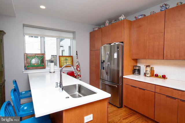 kitchen with brown cabinetry, stainless steel fridge with ice dispenser, a sink, light countertops, and backsplash