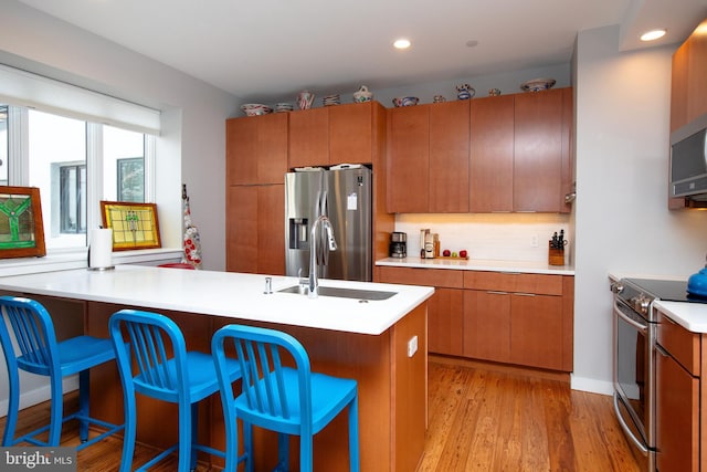 kitchen featuring light countertops, backsplash, appliances with stainless steel finishes, a sink, and light wood-type flooring