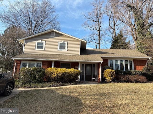 view of front of house featuring a shingled roof, a front yard, and brick siding