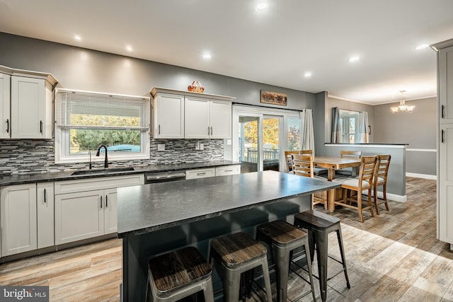 kitchen with a sink, a kitchen bar, decorative backsplash, and light wood finished floors