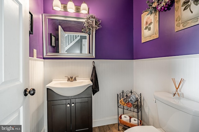 half bathroom featuring vanity, toilet, wood finished floors, and wainscoting