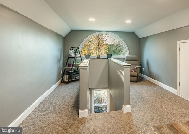 hallway featuring lofted ceiling, carpet, and baseboards