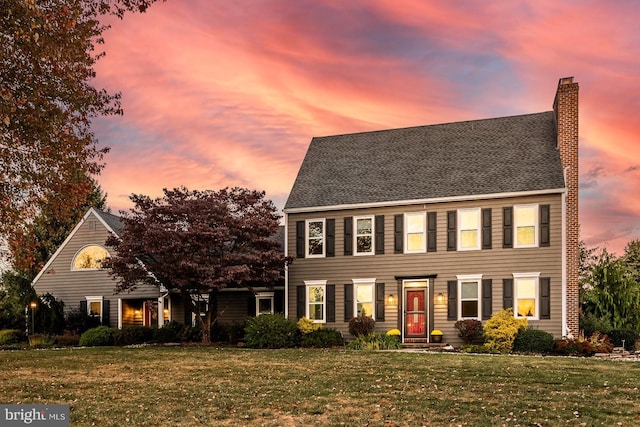 colonial inspired home with a lawn and a chimney