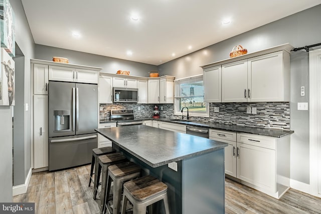 kitchen featuring light wood finished floors, a sink, decorative backsplash, stainless steel appliances, and dark countertops