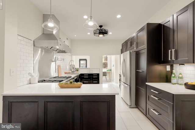 kitchen featuring a peninsula, light countertops, appliances with stainless steel finishes, wall chimney exhaust hood, and decorative light fixtures