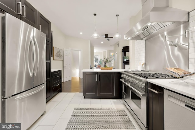 kitchen featuring light tile patterned floors, stainless steel appliances, tasteful backsplash, hanging light fixtures, and wall chimney exhaust hood