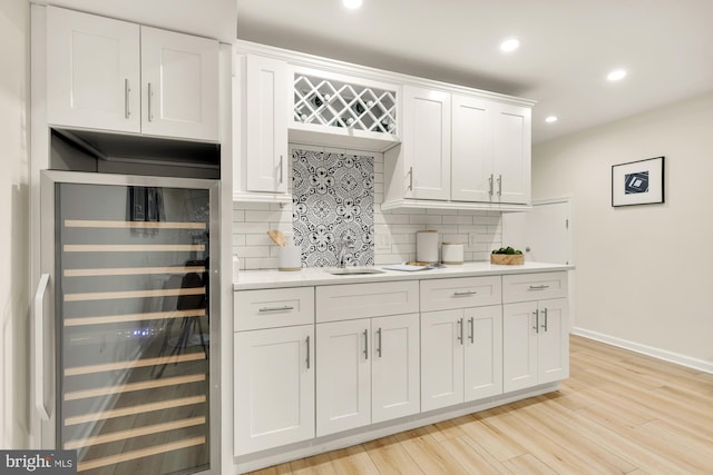 kitchen with wine cooler, white cabinets, light countertops, and backsplash