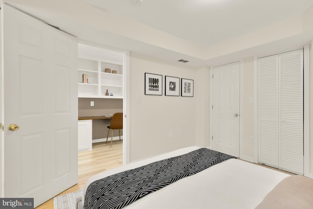 bedroom with light wood-style flooring, visible vents, baseboards, and built in study area