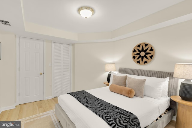 bedroom with visible vents, baseboards, a closet, light wood finished floors, and a raised ceiling