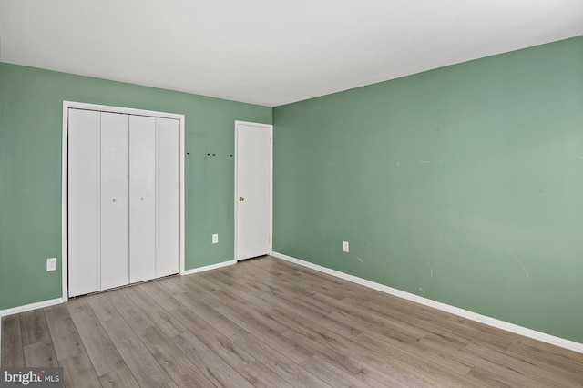 unfurnished bedroom featuring wood finished floors, baseboards, and a closet