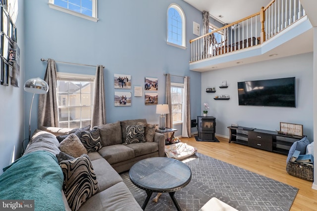 living room with a towering ceiling, wood finished floors, a wood stove, and baseboards