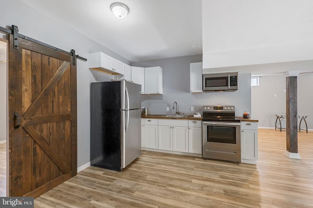 kitchen with a barn door, stainless steel appliances, a sink, white cabinets, and light wood-type flooring