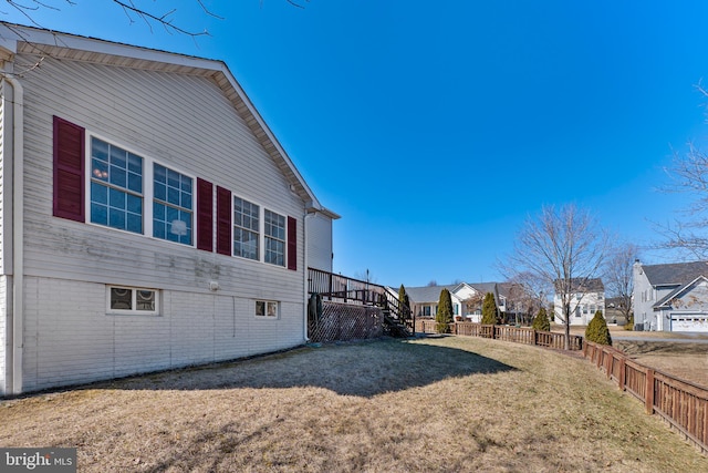 view of side of home featuring a residential view, brick siding, fence, and a lawn