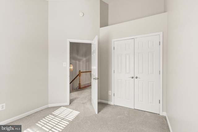 unfurnished bedroom with a high ceiling, a closet, light carpet, and baseboards