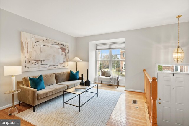 living room with baseboards, a notable chandelier, visible vents, and light wood-style floors