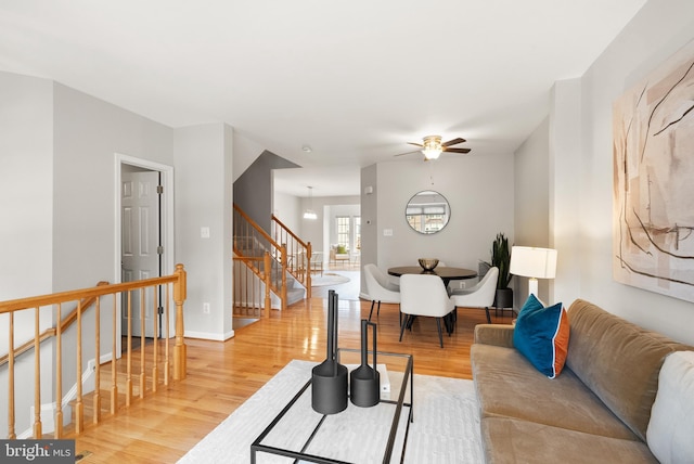 living room featuring stairs, a ceiling fan, baseboards, and wood finished floors