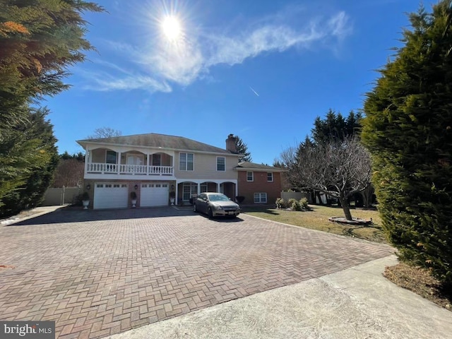 view of front of property with a garage, a balcony, a chimney, and decorative driveway