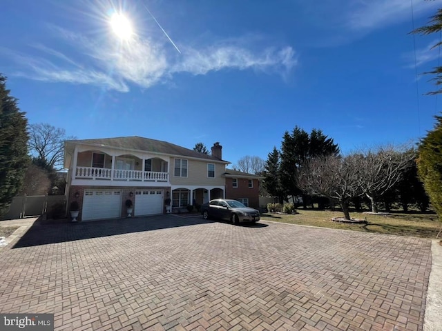 front of property with an attached garage, decorative driveway, a chimney, and a balcony