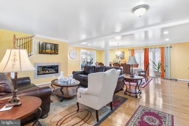 living room featuring baseboards, wood-type flooring, a glass covered fireplace, and crown molding