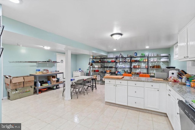 kitchen featuring light stone counters, light tile patterned flooring, a peninsula, white cabinetry, and stainless steel dishwasher