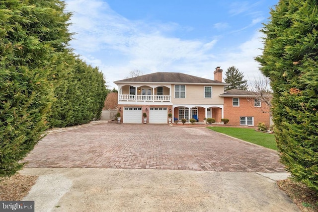 view of front of home featuring decorative driveway, a chimney, a porch, a front yard, and a balcony