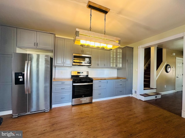 kitchen with glass insert cabinets, appliances with stainless steel finishes, pendant lighting, wood finished floors, and wooden counters